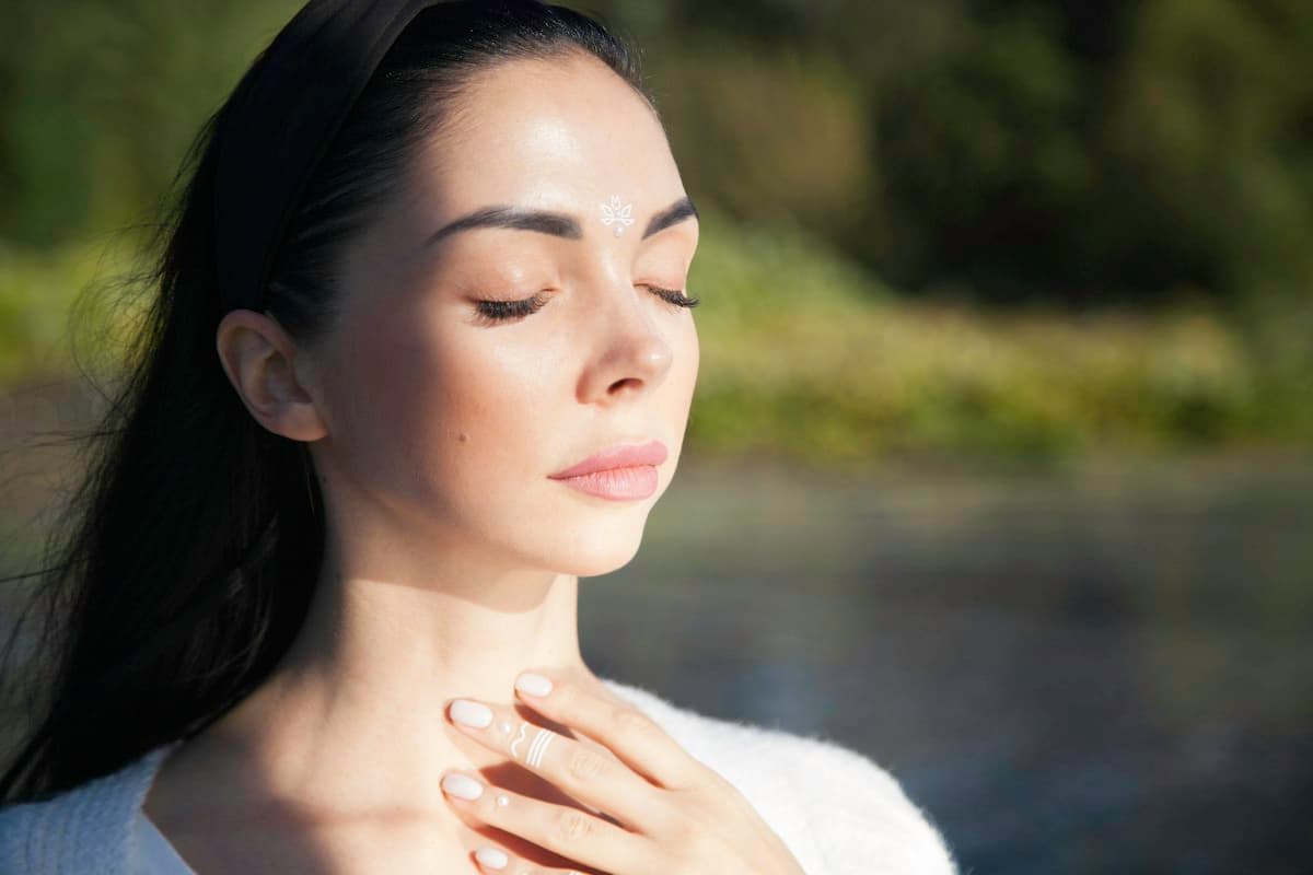 Mujer con los ojos cerrados y una mano sobre el pecho, respirando con calma