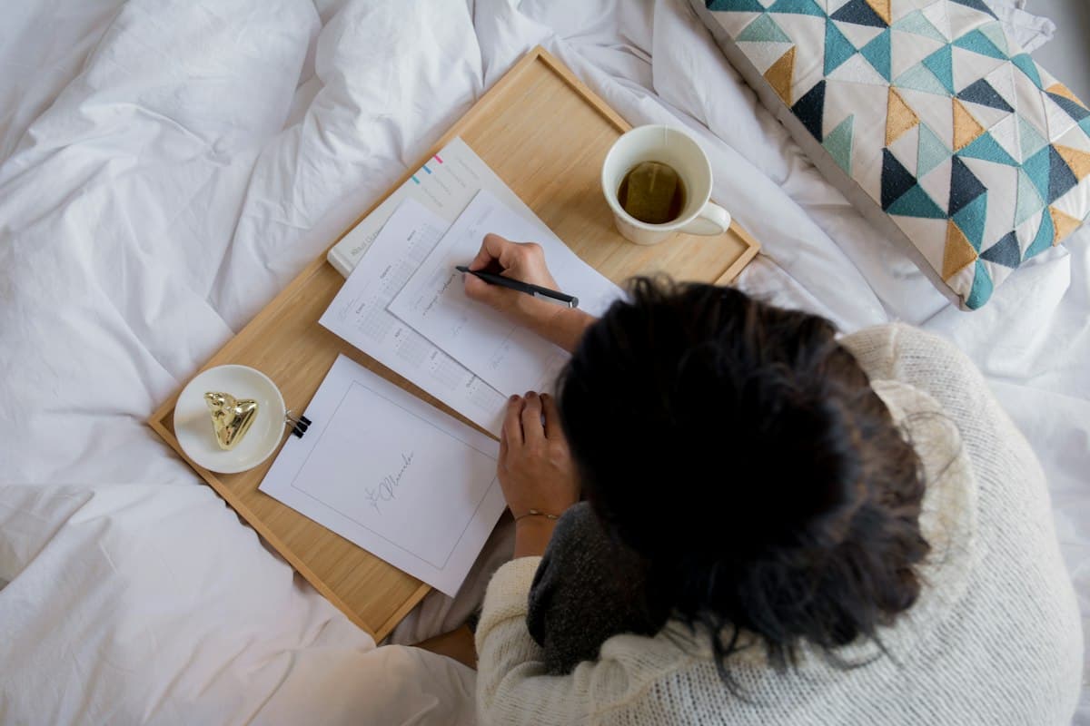 Persona escribiendo en una agenda junto a una taza de té